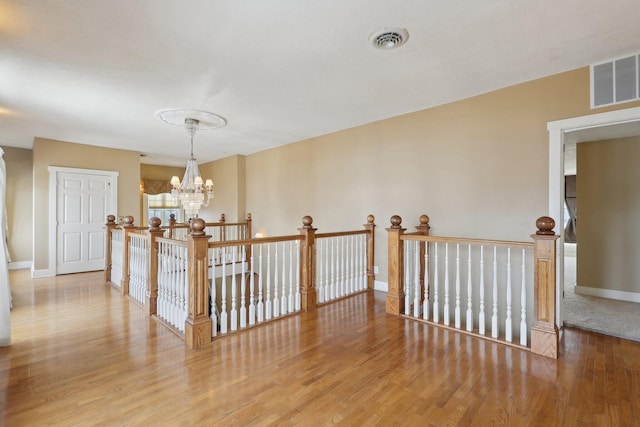 hall featuring light wood-style floors, baseboards, visible vents, and a chandelier