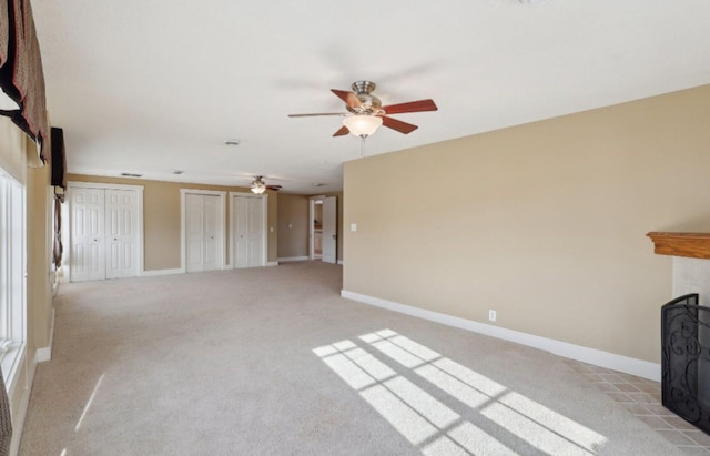 unfurnished living room with light carpet, a fireplace with flush hearth, baseboards, and a ceiling fan