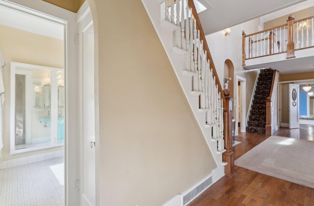 stairs with arched walkways, visible vents, a towering ceiling, wood finished floors, and baseboards