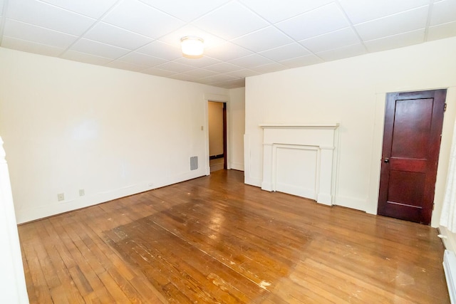 empty room featuring wood-type flooring, a paneled ceiling, and baseboard heating