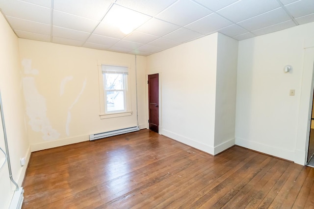 empty room with a baseboard heating unit, hardwood / wood-style floors, and a drop ceiling