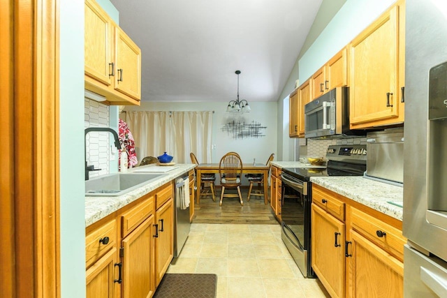 kitchen with tasteful backsplash, hanging light fixtures, appliances with stainless steel finishes, a sink, and light stone countertops