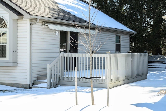 snow covered property with roof with shingles