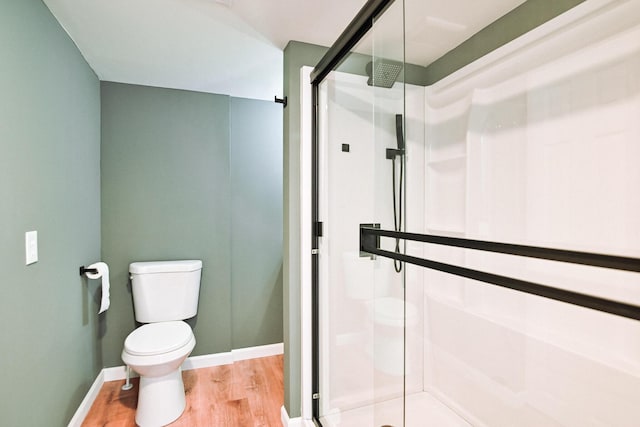 bathroom with a shower stall, toilet, wood finished floors, and baseboards