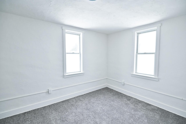 spare room with a wealth of natural light, baseboards, and dark colored carpet