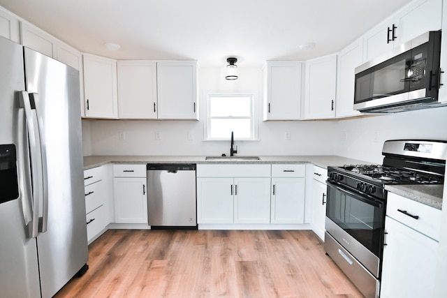 kitchen featuring a sink, white cabinetry, appliances with stainless steel finishes, light wood finished floors, and light countertops