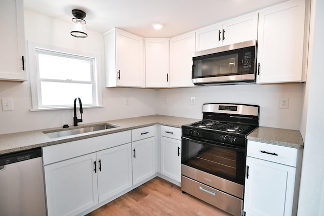 kitchen with light wood finished floors, a sink, stainless steel appliances, light countertops, and white cabinets