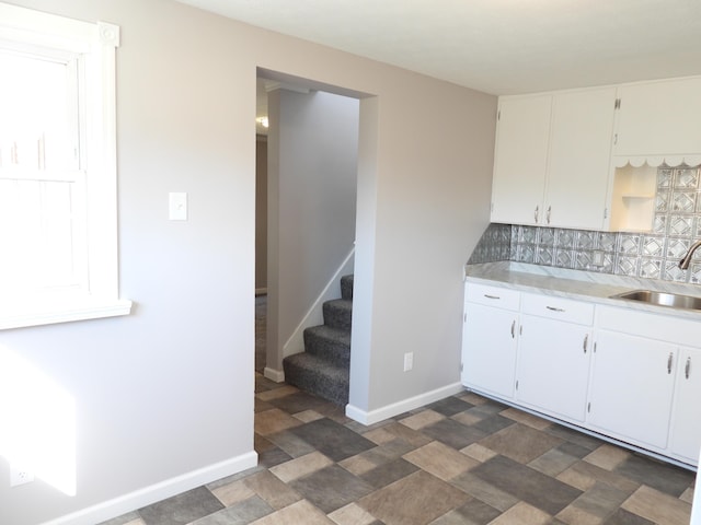 kitchen with stone finish floor, a sink, backsplash, light countertops, and baseboards