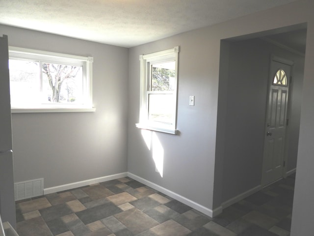 unfurnished room featuring baseboards, visible vents, and a textured ceiling