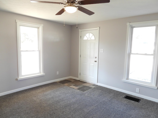 foyer featuring visible vents, plenty of natural light, baseboards, and dark carpet