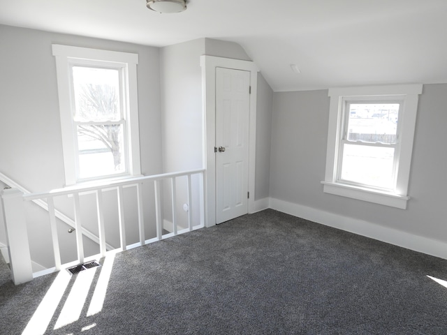 additional living space featuring visible vents, lofted ceiling, a healthy amount of sunlight, and dark carpet