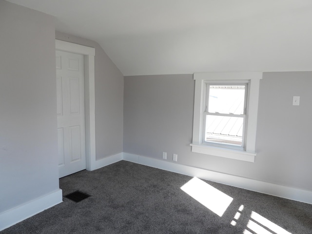 additional living space with dark colored carpet, visible vents, baseboards, and vaulted ceiling