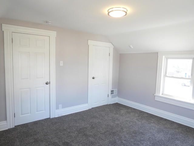 interior space with lofted ceiling, visible vents, dark colored carpet, and baseboards