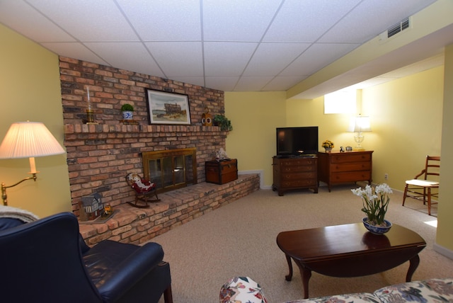 living room with a drop ceiling, a brick fireplace, and carpet floors