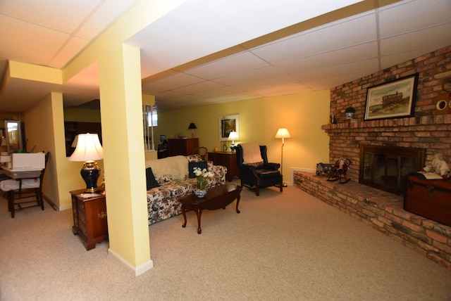 living room featuring a drop ceiling, a brick fireplace, and light carpet