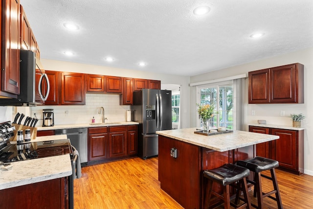 170 Fox Harbor Dr, Troy, OH 45373 - kitchen featuring appliances with stainless steel finishes, dark brown cabinets, a kitchen island, light wood-style flooring, and a textured ceiling