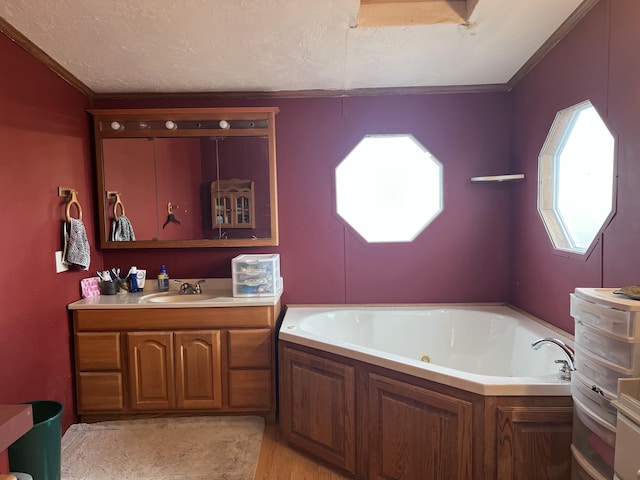 bathroom with a textured ceiling, ornamental molding, vanity, and a bathing tub