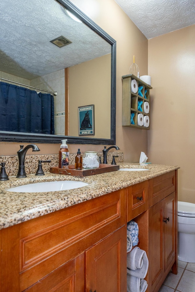 full bath with double vanity, a sink, tile patterned flooring, a textured ceiling, and toilet