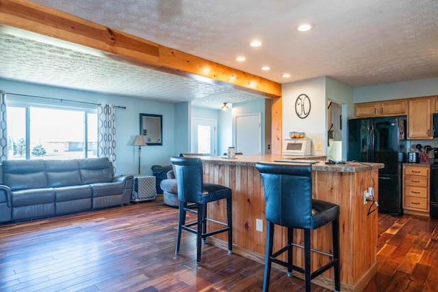 kitchen with a breakfast bar, dark wood-style flooring, freestanding refrigerator, and a textured ceiling