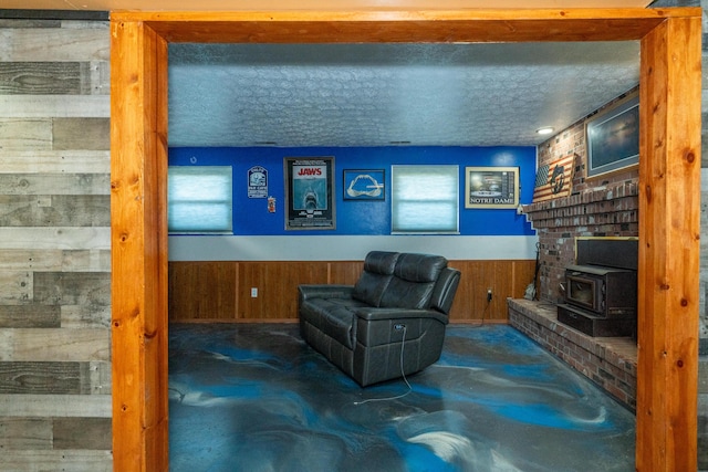 sitting room featuring a wainscoted wall, wooden walls, a textured ceiling, and a wood stove