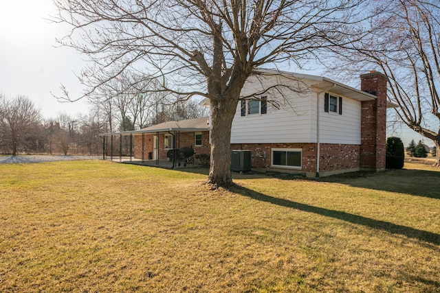 exterior space with brick siding, central AC unit, a lawn, a chimney, and a patio area