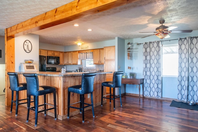 kitchen featuring black appliances, a breakfast bar area, dark wood-style flooring, and a textured ceiling