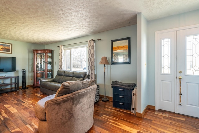 living room with visible vents, wood finished floors, baseboards, and a textured ceiling