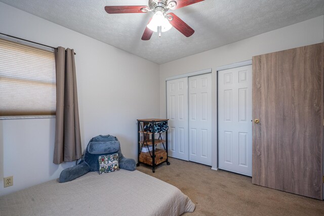 carpeted bedroom with ceiling fan, two closets, and a textured ceiling