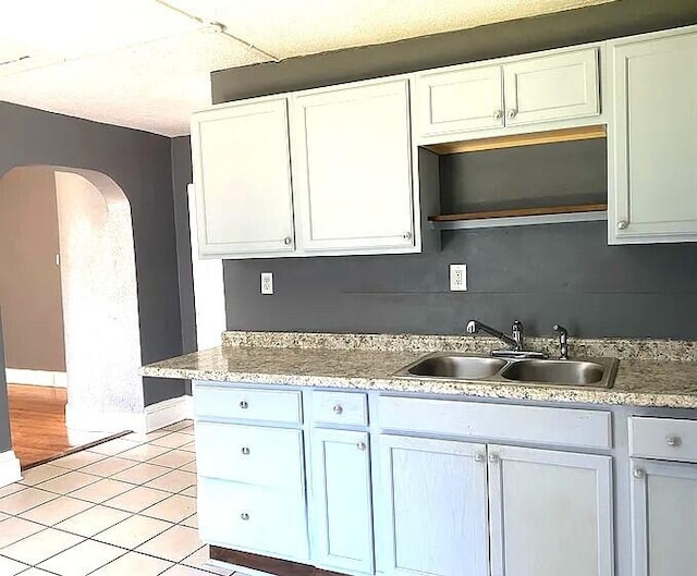 kitchen with arched walkways, light tile patterned floors, a sink, white cabinets, and backsplash