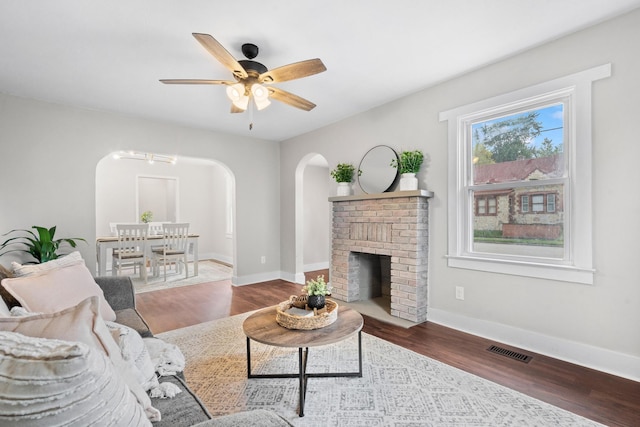 living room with ceiling fan, dark hardwood / wood-style flooring, and a brick fireplace