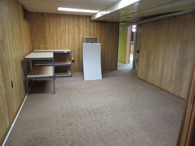 finished below grade area featuring light carpet, wooden walls, and a paneled ceiling