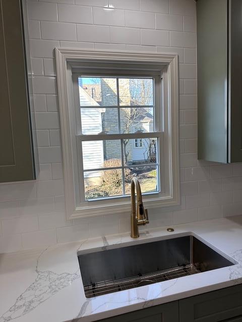 interior details featuring a sink, light stone counters, and backsplash