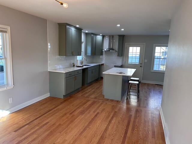 kitchen featuring light wood finished floors, backsplash, gray cabinetry, a kitchen island, and wall chimney range hood