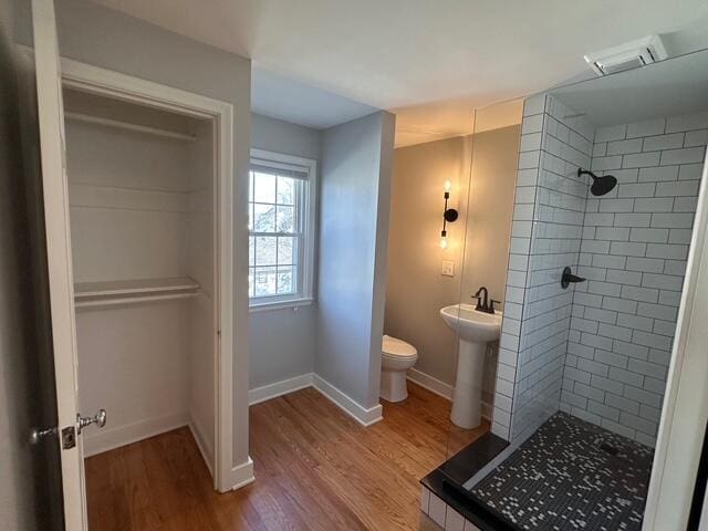 bathroom with baseboards, toilet, a tile shower, wood finished floors, and a sink