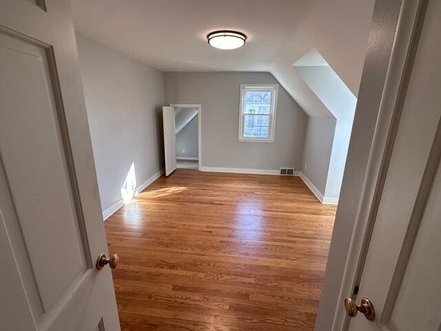 additional living space featuring vaulted ceiling, visible vents, baseboards, and wood finished floors