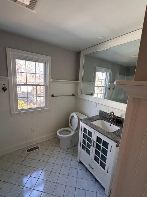 bathroom with tile patterned flooring, visible vents, wainscoting, and toilet