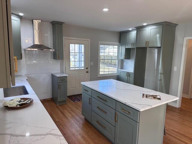 kitchen featuring light stone counters, gray cabinets, wall chimney exhaust hood, and wood finished floors