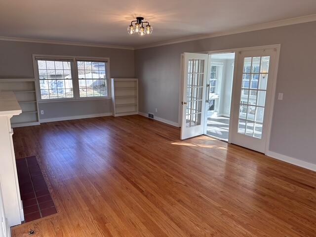 unfurnished living room with a chandelier, wood finished floors, baseboards, and ornamental molding