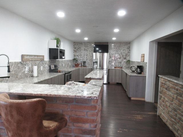 kitchen featuring appliances with stainless steel finishes, dark hardwood / wood-style floors, kitchen peninsula, light stone countertops, and decorative backsplash