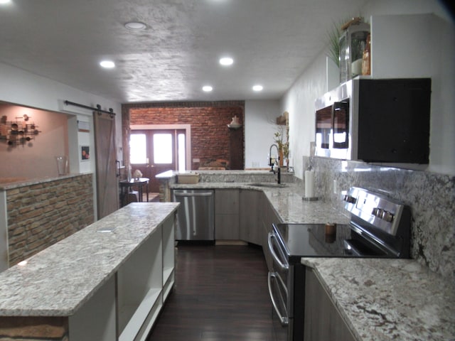 kitchen with sink, dark hardwood / wood-style flooring, a barn door, stainless steel appliances, and light stone countertops