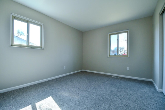 spare room with visible vents, a healthy amount of sunlight, baseboards, and dark colored carpet