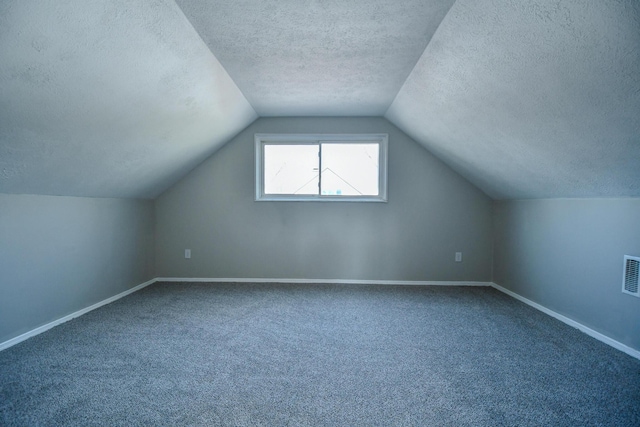 additional living space with baseboards, visible vents, dark carpet, and a textured ceiling