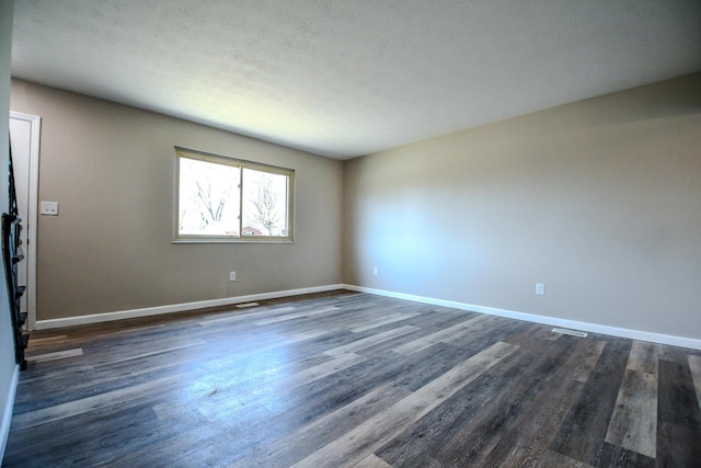 empty room featuring visible vents, baseboards, and dark wood-style floors