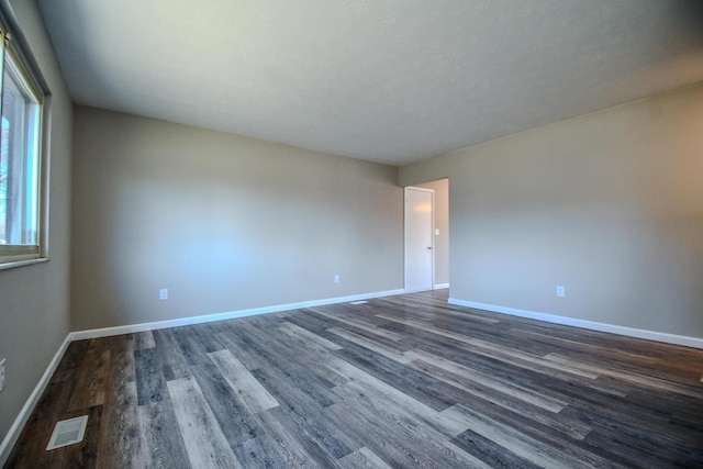 unfurnished room with visible vents, baseboards, and dark wood-style flooring