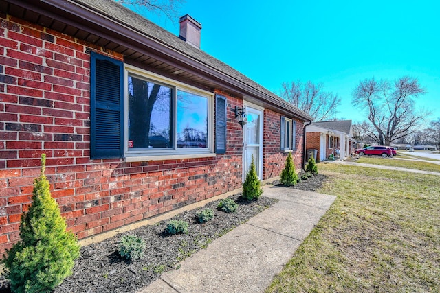 view of side of property featuring a yard, brick siding, and a chimney