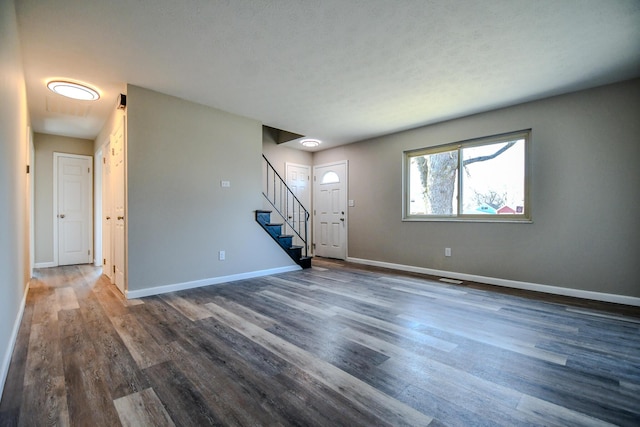 unfurnished living room with stairway, baseboards, visible vents, and wood finished floors