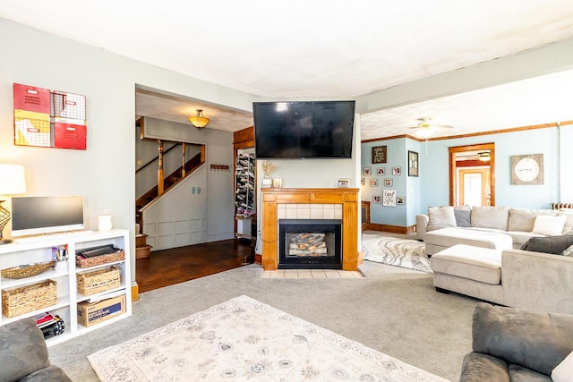 carpeted living area with a tiled fireplace, stairway, and a ceiling fan