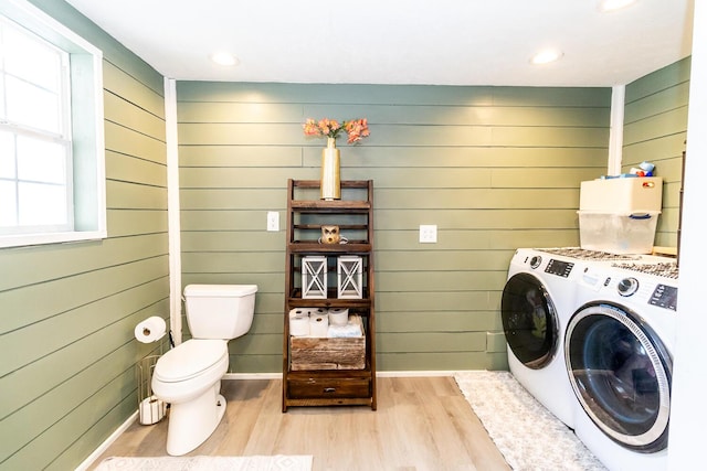 clothes washing area featuring wooden walls, wood finished floors, washing machine and clothes dryer, laundry area, and baseboards