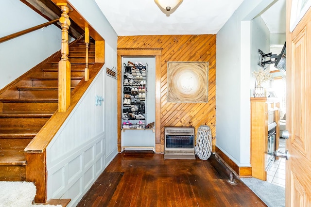 staircase featuring hardwood / wood-style floors, heating unit, wood walls, and a fireplace