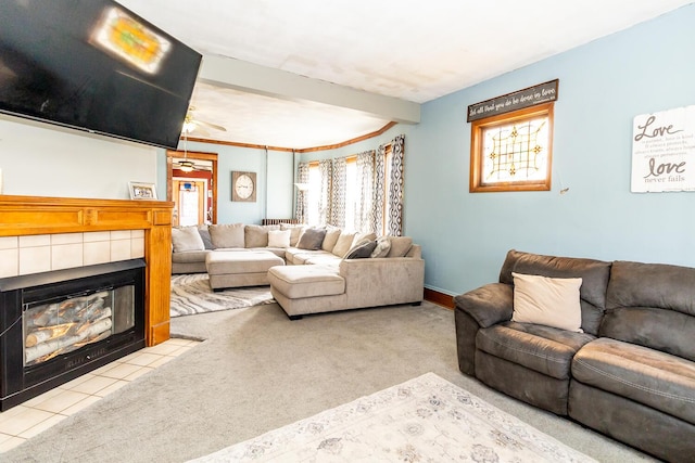 living area featuring a ceiling fan, carpet floors, a tile fireplace, and beamed ceiling